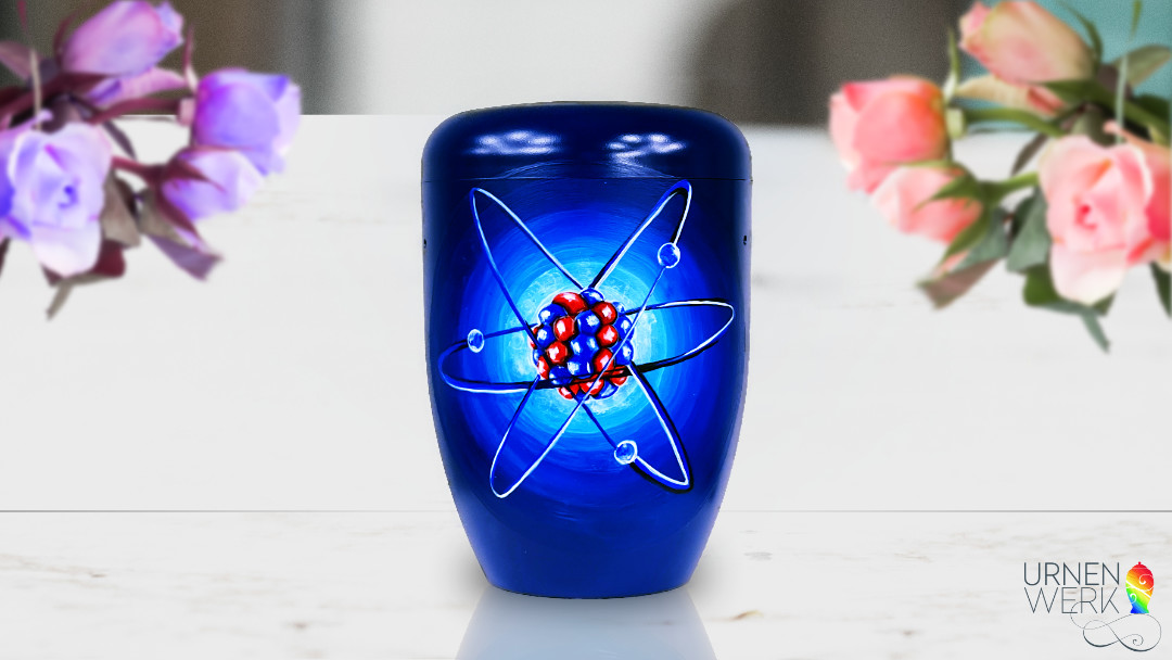 Die dunkelblaue Urne mit dem Atom in Blau und Rot steht auf einem Tisch. Links und Rechts befinden sich Blumen.