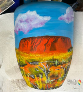 Die fertige Ayers Rock mit Wolken und Gräsern und trockenen Bäumen.