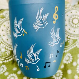 Die türkise Urne mit weißen Tauben sowie schwarzen und weißen Musiknoten. Goldene Notenschlüssel verzieren die Urne.